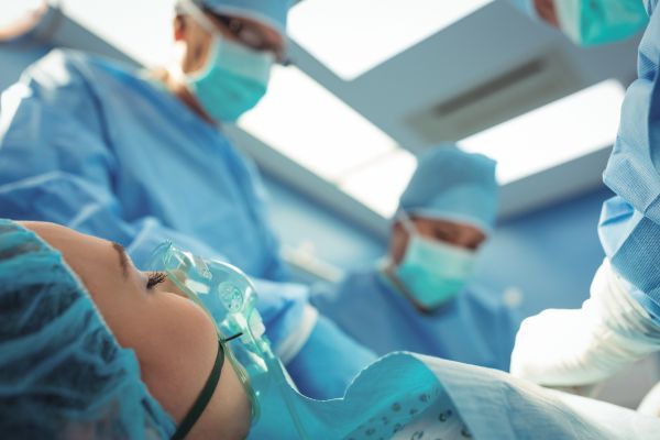 A seleção do tipo de anestesia representa uma etapa crucial na preparação para procedimentos médicos, sendo determinada pela natureza específica da cirurgia e pelas necessidades individuais do paciente. Cirurgiões preparando uma paciente para cirurgia.