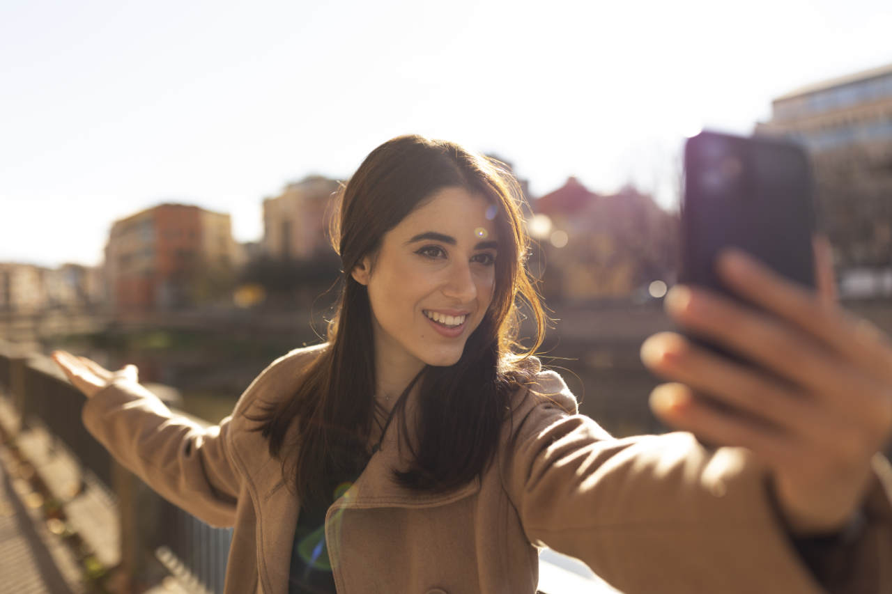 Jovem mulher tirando selfie com câmera frontal do celular