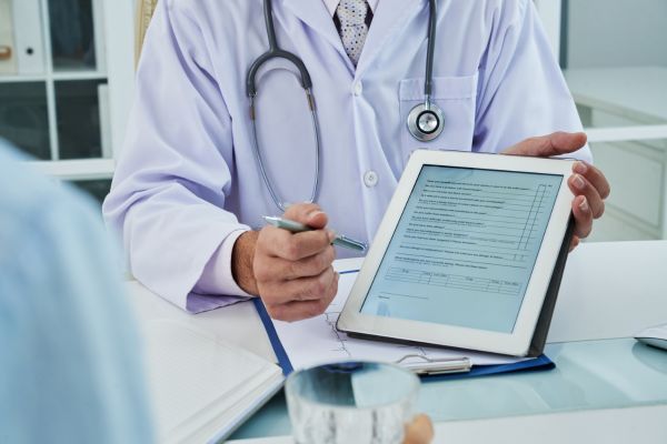 Consulta médica com o médico mostrando uma tabela digital para o paciente.